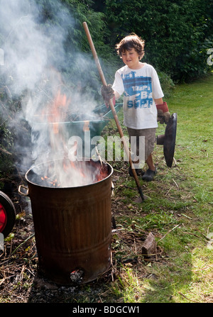 Jeune garçon de 7 ans dans des déchets de jardin en feu avec de la fumée de l'incinérateur qui ondulent. Banque D'Images