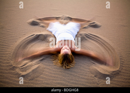 Une femme en blanc faisant un ange de sable sur les Dunes de Stovepipe Wells dans la vallée de la mort, en Californie. Banque D'Images