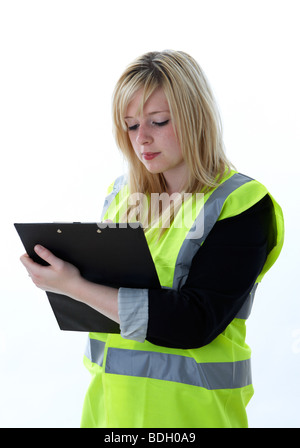 Jeune femme blonde de 20 ans portant un gilet haute visibilité se concentrant sur l'écriture d'un presse-papiers Banque D'Images