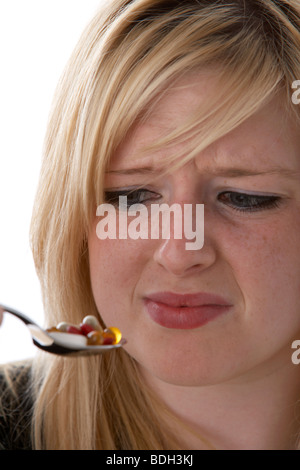 Jeune femme blonde de 20 ans avec une cuillerée de suppléments de vitamine à dégoûté Banque D'Images