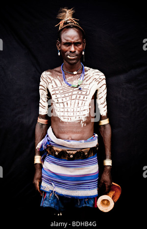 Portrait d'un homme en costume traditionnel et décoration corps posés devant un tissu noir. Banque D'Images