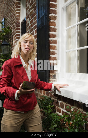 Une femme se tient à côté d'une chambre avec fenêtre une brique dans sa main, Charleston, Caroline du Sud, USA Banque D'Images