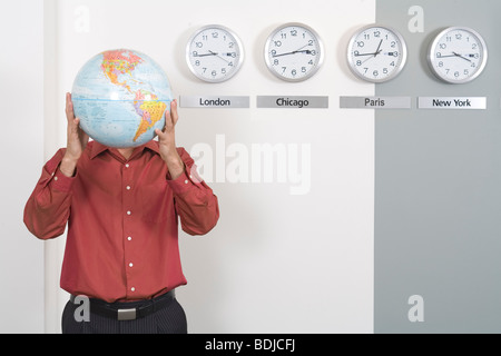 Businessman Holding Globe debout par Clocks Showing fuseaux internationaux Banque D'Images