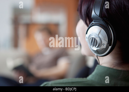 Close-up of Woman Wearing Headphones, Man Reading dans l'arrière-plan Banque D'Images