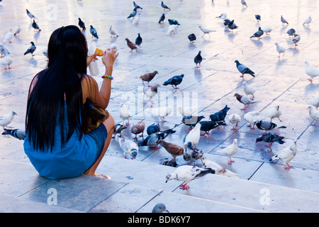 Ville de Valence , Espagne , Plaza de la Virgen , jolie jeune fille oriental avec de longs cheveux noirs s'assoit sur les marches & rss pigeons Banque D'Images