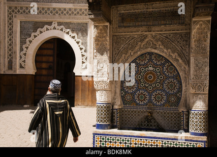 Fes, Maroc, l'homme en costume traditionnel en passant devant une fontaine décorative Banque D'Images