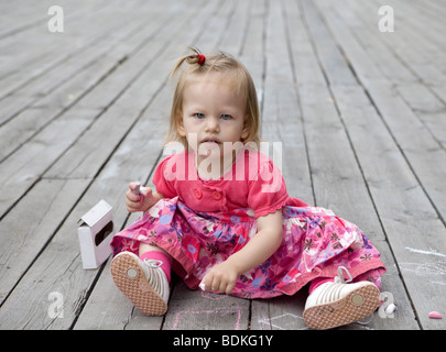 Petite fille mignonne deux ans attire par la craie sur plancher en bois Banque D'Images