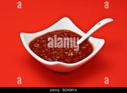 Sauce Chili dans un plat blanc avec cuillère de service sur fond rouge Banque D'Images