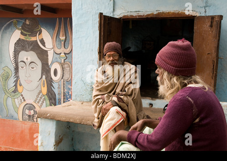 Les hommes Indiens barbu s'asseoir et parler à côté d'un lieu de culte à Varanasi, Inde. Une peinture du dieu hindou Shiva peut être vu (à gauche). Banque D'Images