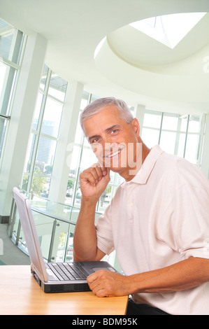 Smiling Mature Woman assis à l'ordinateur vu de côté dans la configuration de bureau Banque D'Images