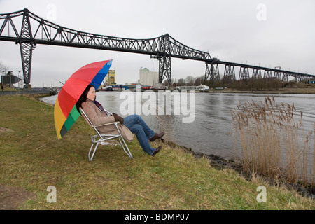 Jeune femme, de 30 à 35 ans, assis au Canal de Kiel et d'attente pour les navires de passage par temps froid, Rendsburg, Schleswig-Holstei Banque D'Images
