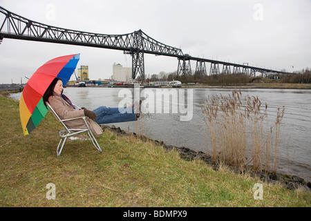 Jeune femme, de 30 à 35 ans, assis au Canal de Kiel et d'attente pour les navires de passage par temps froid, Rendsburg, Schleswig-Holstei Banque D'Images