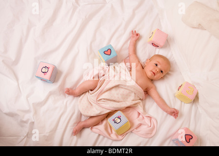 A deux mois, bébé fille est enveloppée dans une couverture et est entouré par quelques-uns de ses jouets. Banque D'Images