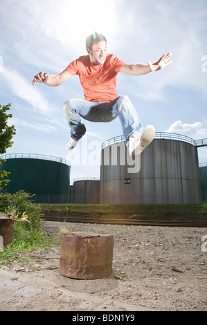 Jeune homme de sauter devant un site industriel Banque D'Images