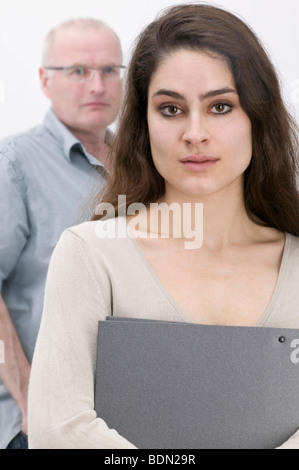 Girl holding un fichier, de sérieux à l'homme à l'arrière Banque D'Images