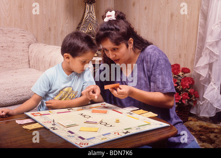 Latina mère garçon apprend comment jouer au Monopoly croître voir démontrer Banque D'Images