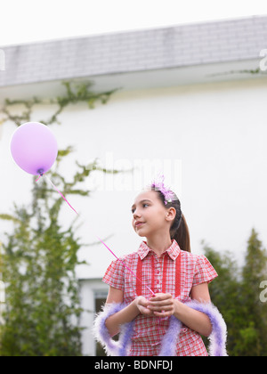 Girl (10-12) en plume boa holding balloon outside house Banque D'Images