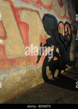 Scooter l'ombre et graffiti sur mur en ville ville Banque D'Images