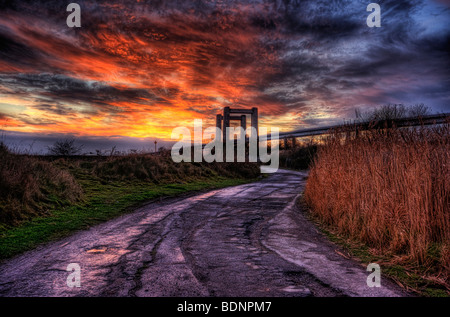 Burnt red soir ciel coucher de soleil sur les pentes de la rivière. Les nouveaux et les anciens ponts swale sur horizon et sinueuse route qui mène jusqu'à des ponts Banque D'Images