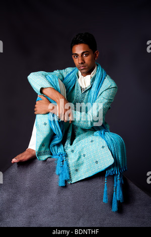 Belle homme hindou indien authentique typique de vêtements ethniques groom assis détendu sur top rock appuyée sur le genou. Bangali homme Banque D'Images