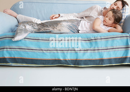 Jeune fille (5-6) wearing costume de sirène de dormir sur un canapé avec la mère Banque D'Images