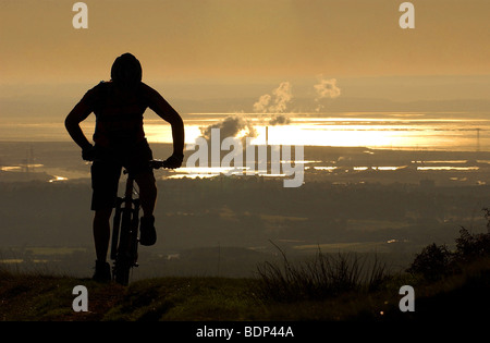 Un cross-country de vélo de montagne grimpe en silhouette comme le soleil se lève sur Newport, Pays de Galles et le Canal de Bristol Banque D'Images