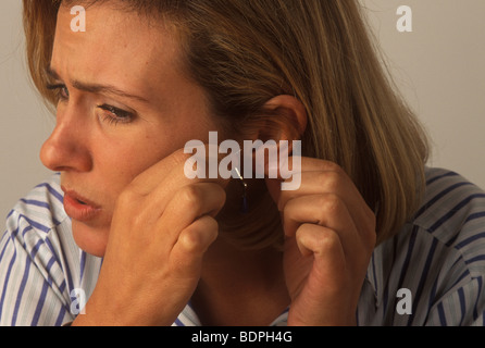 Femme avec une inflammation de l'oreille qui démange souffrant d'une allergie au nickel Banque D'Images