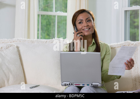 Hispanic woman working on a laptop and talking on a mobile phone Banque D'Images