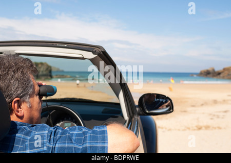 Homme mûr assis dans un cabriolet à la mer binoculars, Cornwall UK Banque D'Images