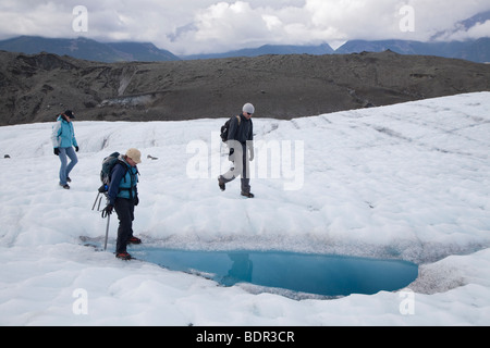 Kennicott, Alaska - Randonneurs sur le glacier en racine Wrangell-St. Elias examiner une piscine d'eau de fonte. Banque D'Images
