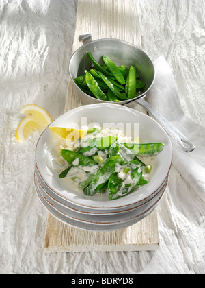 Les pois mange-tout avec sauce au citron et des tranches de citron pour presser dans une pile de plats en faïence Banque D'Images