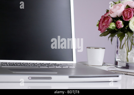 L'argent de l'ordinateur portable sur un bureau avec un espresso, un stylo, et d'un vase avec de belles fleurs roses et blanches à côté. Banque D'Images