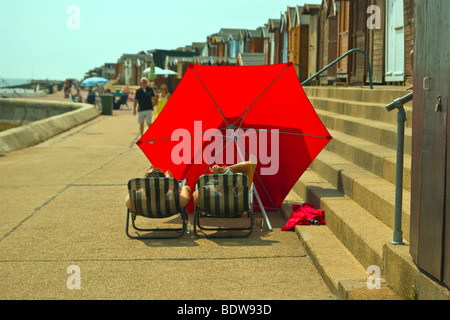 Conscient de la santé Couple détendez vous sous leur parasol dans le soleil de midi dans la région de Walton sur th UK Angleterre Essex  ? Banque D'Images