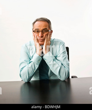 Manager avec des lunettes assis à un bureau, appuyant sa tête fatiguée avec ses mains Banque D'Images