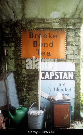 Signes d'étain ancien thé Brooke Bond et étrave cigarrettes sur un mur humide avec godet et RDP, la paraffine peut, arrosoir, etc. Banque D'Images