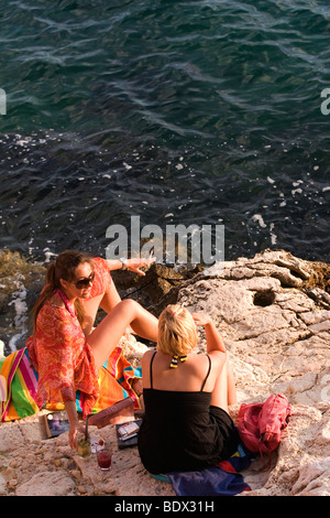 Deux femmes prendre un verre et une cigarette sur les rochers dans la marina de Rovinj Croatie Banque D'Images