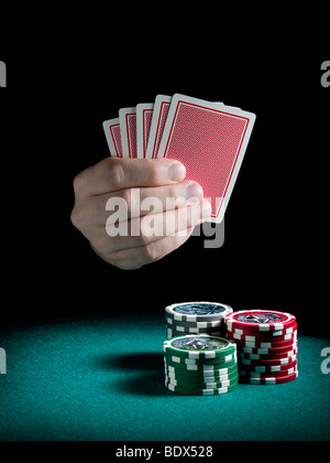 La main d'un homme détenant cinq cartes sur trois piles de jetons de différentes couleurs sur un feutre vert. Banque D'Images