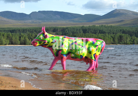 Une vache rose fluorescent et de chaux sur une planche de surf à Loch Morlich, avec les Cairngorms au loin. Banque D'Images