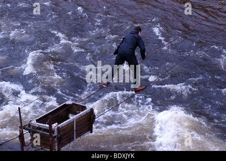 Randonneur aventureuse traversée par le col de câbles métalliques d'un pont de corde à Glen Etive, Écosse, Royaume-Uni, Europe Banque D'Images