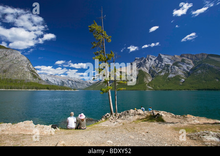 Jeune couple assis sur le rivage rocheux. Le lac Minnewanka, Banff National Park, Alberta, Canada. Banque D'Images