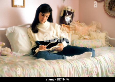Une adolescente blanche ne travail scolaire dans sa chambre se reposer sur des oreillers lit Banque D'Images