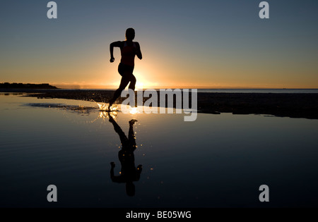 Young Woman Running on Beach at Sunset Banque D'Images