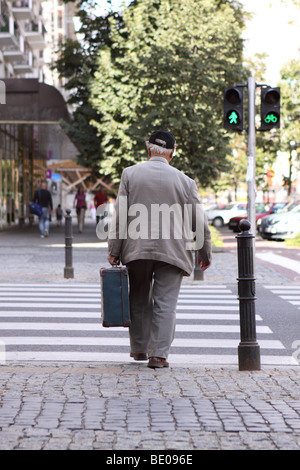 Un homme âgé portant une valise balade dans une ville à l'aide d'un passage à niveau un homme vert MODÈLE PAS SEULEMENT UTILISATION ÉDITORIALE PARUTION Banque D'Images