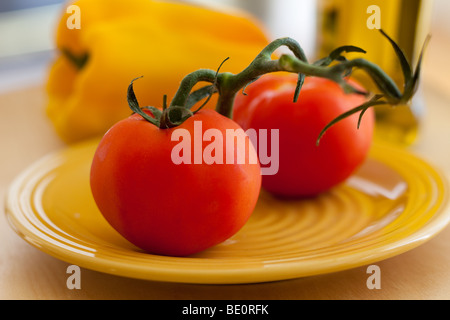 Succulentes tomates rouges frais avec vigne sur plaque jaune Banque D'Images