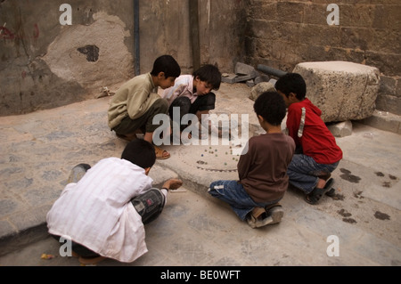 Un groupe de cinq garçons yéménite jouant un jeu de billes dans un cul-de-sac dans les rues du vieux Sanaa, Yémen. Banque D'Images