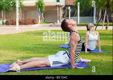 L'homme et de la femme faisant du yoga à l'extérieur dans le parc Banque D'Images