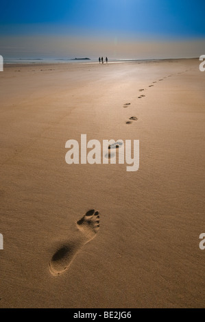 Pas dans le sable sur une plage dorée avec un groupe de personnes au loin Banque D'Images