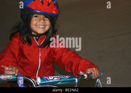 Trois ans, fille, sourire et faire de la bicyclette, le port d'un casque Banque D'Images