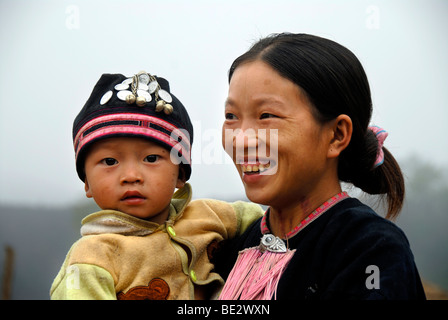 La pauvreté, portrait, l'ethnologie, Yao femme vêtue d'un costume traditionnel, souriant avec un bébé dans les bras, village de Ban Houey Banque D'Images