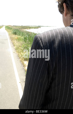 Regarder par-dessus l'épaule d'un homme en costume rayé marchant dans un sentier du littoral Banque D'Images